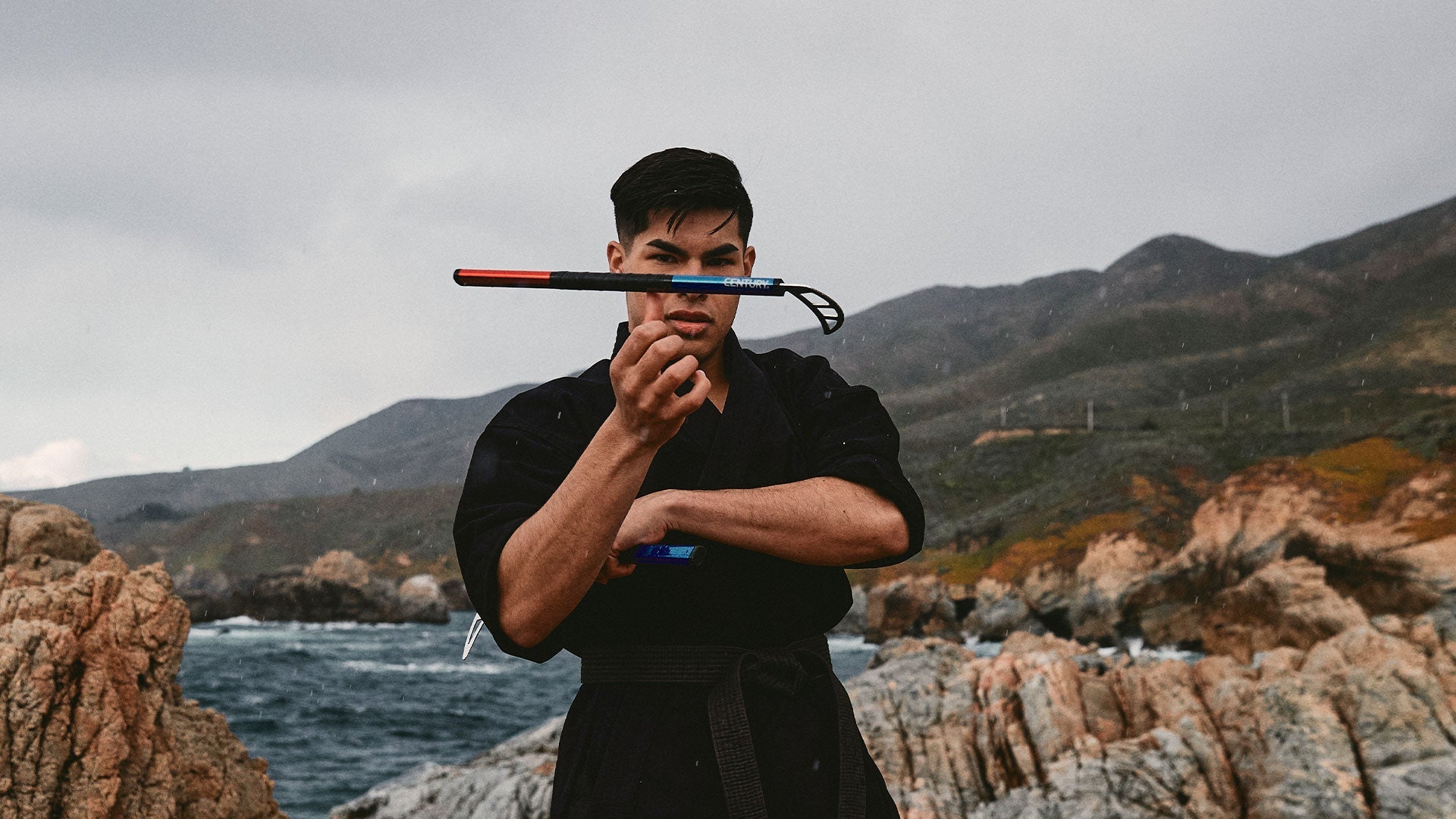 man posing with martial arts weapon near ocean